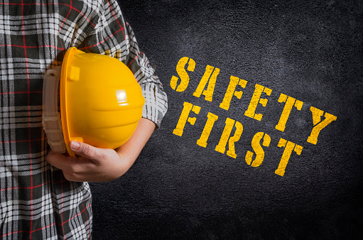 Safety first concept. Safety first stencil print on the black concrete wall. Construction worker with yellow safety helmet.