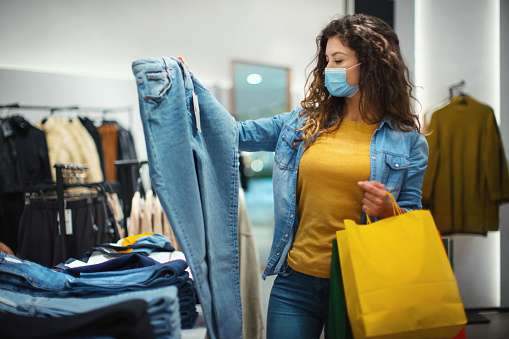 Closeup side view of a late 20's woman choosing some clothes at a shopping mall buying some jeans after reopening during coronavirus pandemic.