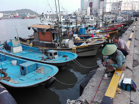 Dadaepo, Busan, South Korea, September 8, 2017: Two men fishing on a pier next to the boats in Dadaepo Fisherman's Port, Busan