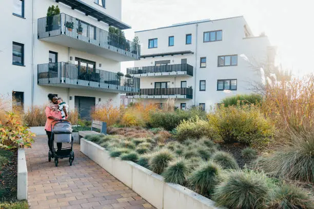 Mother pushes her stroller on a path through townhouses in autumn