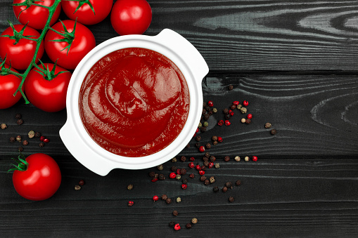 ketchup in a plate with red tomatoes, round peppers and bay leaves on a black wooden background. Making ketchup