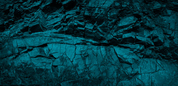 istock Blue rocky stone background. Monochrome dark turquoise toned rock texture. Weathered crumbling mountain surface. Close-up. 1283846076
