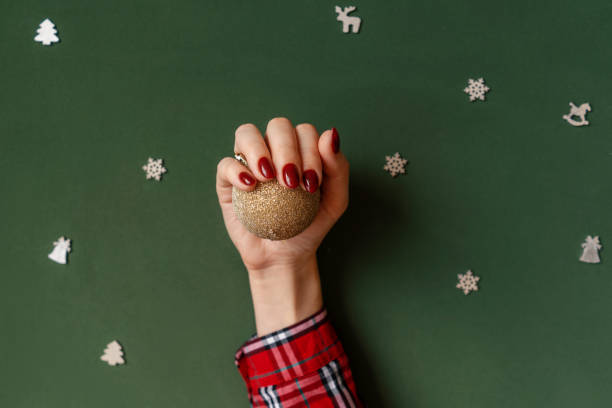 Christmas manicure. Red nails on green background. Christmas manicure. Red nails, hands in checkered shirt hold golden ball on green background with silver baubles. christmas nails stock pictures, royalty-free photos & images