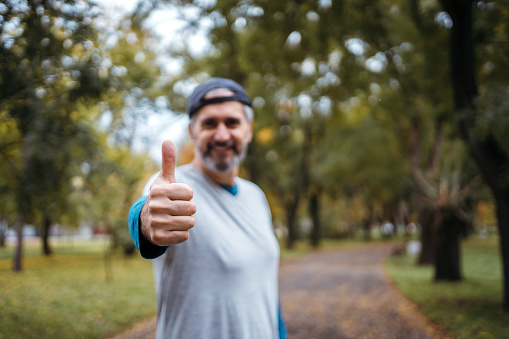 Smiling man showing thumb up and looking at camera in the park.