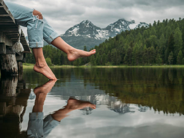 Feet dangling from lake pier One person on wooden lake pier relaxing and enjoying mountain lake scenery barefoot stock pictures, royalty-free photos & images