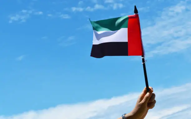 Photo of United Arab Emirates UAE national day with hand holding flag against blue sky