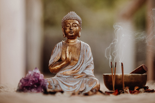 Close up of a Buddha figurine and smoky incense with gong and amethyst. Focus on the Buddha and the incense.