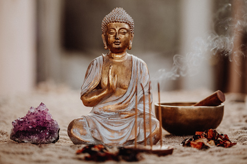 Close up of a Buddha figurine with incense, gong, dried leaves and amethyst. Focus on the Buddha figure.