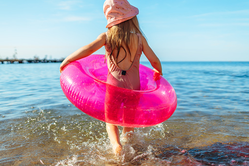 Happy little girl bathing in sea with pink circle and hat