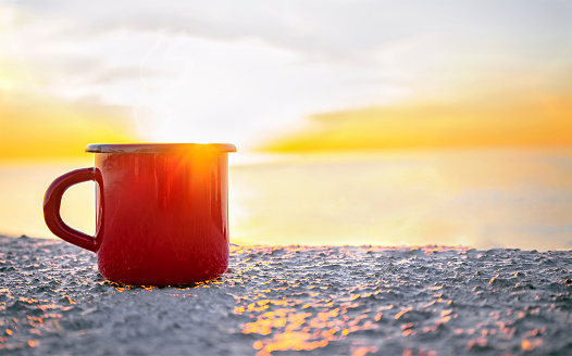 Good morning sunrise concept. Red mug with tea or coffee on the beach with sea on background. Sunlight and sunrise. Lets start a new day. Space for text