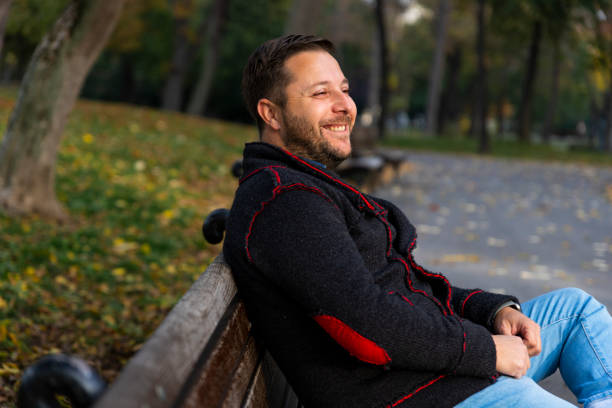istock Smiling man sitting on the bench in the park at autumn 1283853968