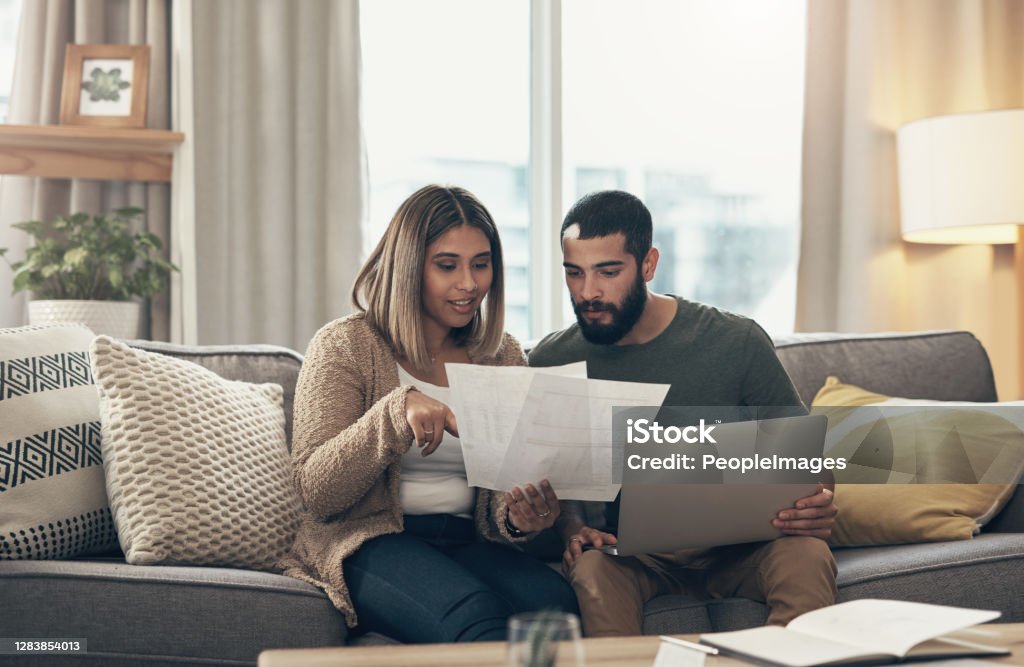 It takes two to make our budget work Shot of a young couple using a laptop while going through paperwork at home Couple - Relationship Stock Photo