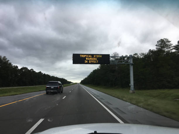 Driver view down largely empty interstate leading to storm-impacted area, with menacing clouds overhead and an electrical information sign above the travel lanes. Photo taken in northwest Florida, the day after Hurricane Sally moved through the area. Shot on iPhone 6S Plus