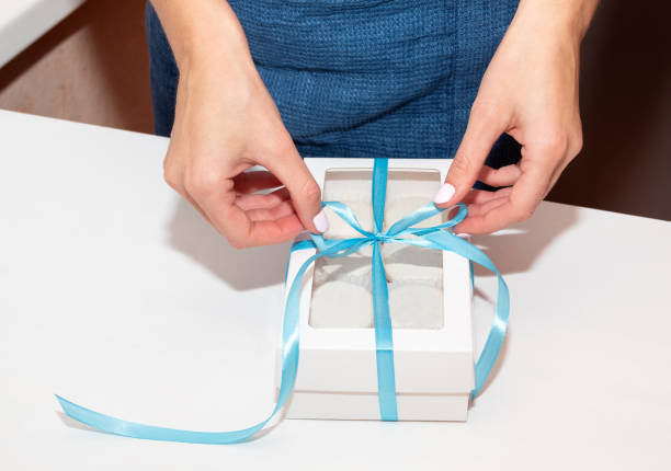 istock Hands tie a blue bow on a box of macaroons. Handmade gift for a holiday. 1283857112