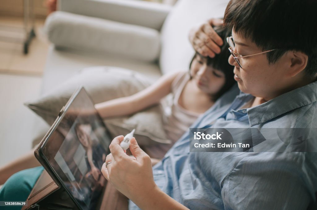 Telemedicine telehealth asian chinese mother using digital tablet communicate with doctor pediatrician on her daughter sickness after taking her daughter temperature Telemedicine telehealth asian chinese mother using laptop communicate with doctor pediatrician on her daughter sickness Telemedicine Stock Photo