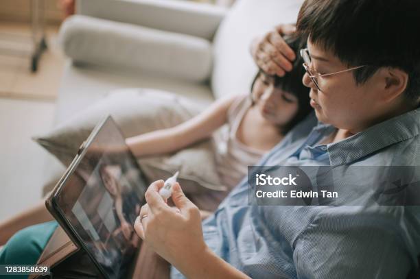 Telemedicine Telehealth Asian Chinese Mother Using Digital Tablet Communicate With Doctor Pediatrician On Her Daughter Sickness After Taking Her Daughter Temperature Stock Photo - Download Image Now