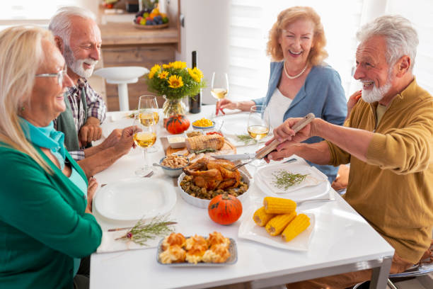 Elderly man cutting chicken while having Thanksgiving dinner with friends