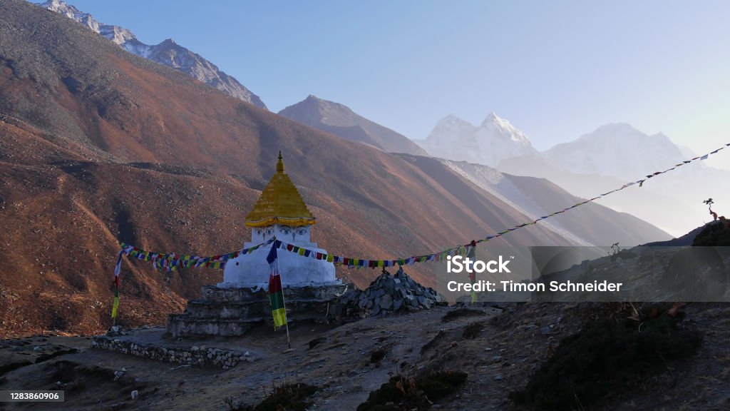 Buddhist monument (chorten) surrounded by mani stones and colorful prayer flags in the bright evening sun in Dingboche, Khumbu, Nepal in the majestic Himalayas. Buddhist monument (chorten) surrounded by mani stones and colorful prayer flags in the bright evening sun in Dingboche, Khumbu, Nepal on Everest Base Camp Trek in the majestic Himalayas. Mt. Everest Stock Photo