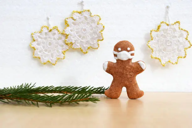 Gingerbread man with protective face mask, spruce twig and crocheted decoration in background. Creative concept in coronavirus (COVID-19) time