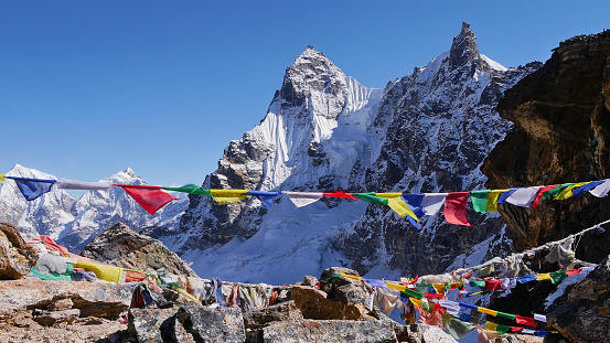 Colorful Buddhist prayer flags peacefully waving in the cold wind on the summit of Renjo La pass, Himalayas, Nepal with ice-capped mountains in background on the Three Passes Trek.