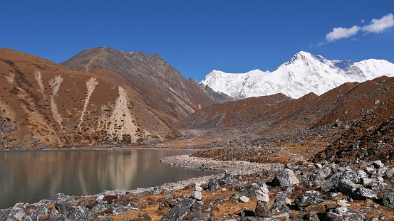 Craggy rock field at the shore of Second Lake on Three Passes Trek in Gokyo valley, Khumbu region, Himalayas, Nepal with majestic ice-capped mountain Cho Oyu (summit 8,188 m) in background.