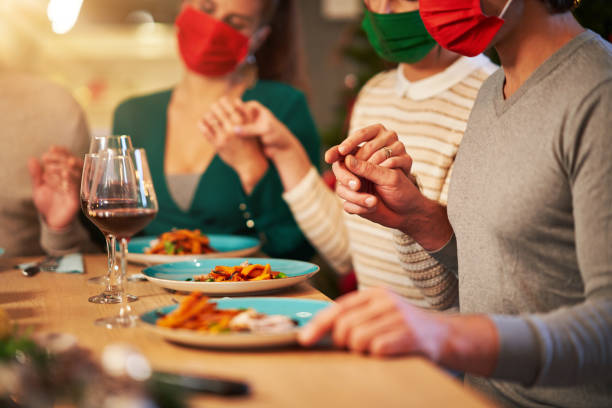 Group of friends in masks praying over Christmas Thanksgiving table at home Picture showing group of friends wearing masks praying over Thanksgiving Christmas table at home thanksgiving holiday covid stock pictures, royalty-free photos & images