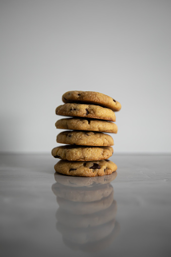 A front angle shot of a stack of chocolate chip cookies reflecting in a grey marble kitchen counter top.
