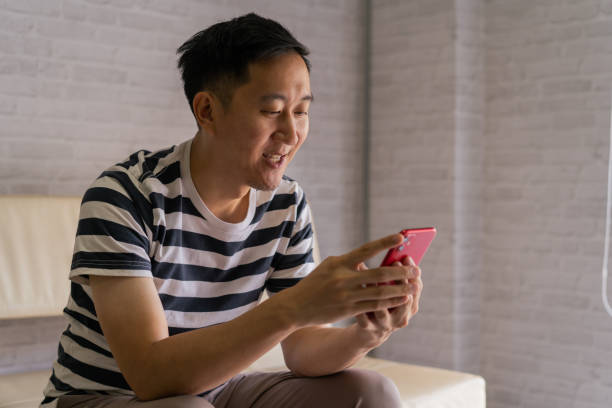 istock Asian man holding smart phone on his hands with copy space at home and sitting on sofa 1283864774