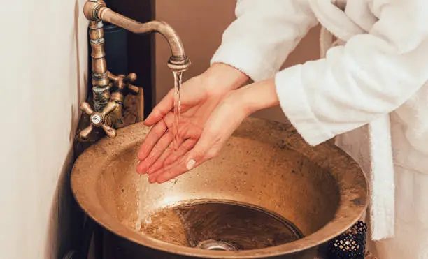 Photo of Washing hands, a woman in a bathrobe washes her hands in the wash basin. Vintage washbasin and woman hands closeup