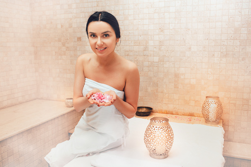 Cheerful woman with rose petals in hands, sitting in a Turkish hammam. Traditional turkish bath