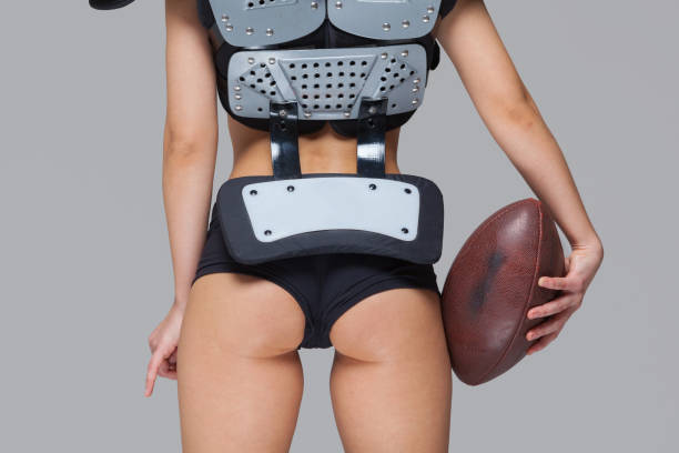 Young sporty brunette wearing sexy uniform of American football player posing with ball looking at camera isolated on grey background Young sporty brunette wearing sexy uniform of American football player posing with ball looking at camera isolated on grey background. sex symbol stock pictures, royalty-free photos & images