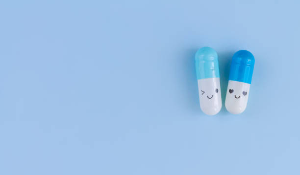 Two capsules with funny faces on blue background top view Two white and blue capsules with funny faces on blue background top view capsule pill no people smiley face stock pictures, royalty-free photos & images