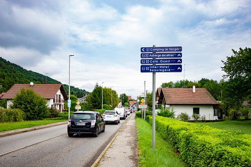 A view of the traffic heading towards the Lake at Annecy, France, with the Alps visible through the low cloud. In the foreground is a sign giving directions to the tourist spots in the town,