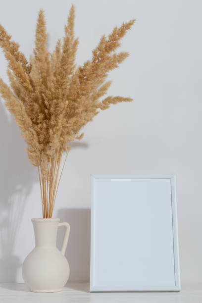 istock A vase with yellow spikelets and a white photo frame on the table. Light stylish background. Preparation for inscriptions, copy space. 1283883321
