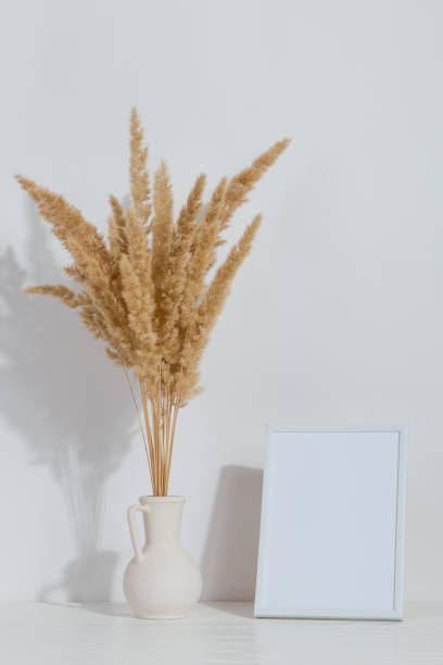 istock A vase with yellow spikelets and a white photo frame on the table. Light stylish background. Preparation for inscriptions, copy space. 1283883326