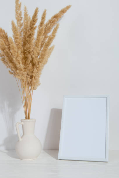 istock A vase with yellow spikelets and a white photo frame on the table. Light stylish background. Preparation for inscriptions, copy space. 1283883328