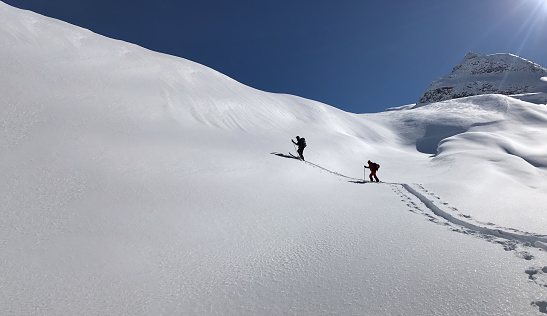 Two skiers climbing upward to the top. Blue sky and cold fresh snow.
