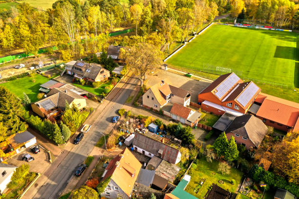 vista aérea del borde de un pueblo con casas privadas y un campo deportivo con un campo de fútbol verde con césped en la esquina - aerial view building exterior suburb neighbor fotografías e imágenes de stock