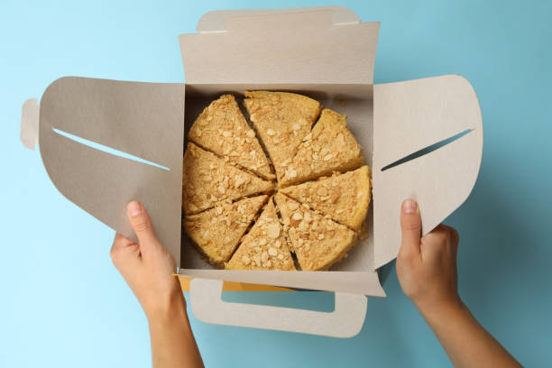 les mains femelles tiennent la boîte de livraison avec le gâteau de napoléon sur le fond bleu - cake box packaging recycling photos et images de collection