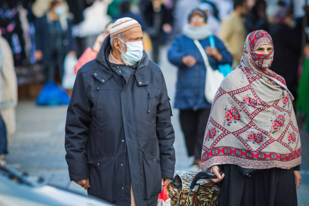 ロンドンのウォルサムストウ市場で買い物をしている間、マスクとヒジャーブを覆う顔をしているイスラム教徒の男女(bameコミュニティ) - muslim cap ストックフォトと画像