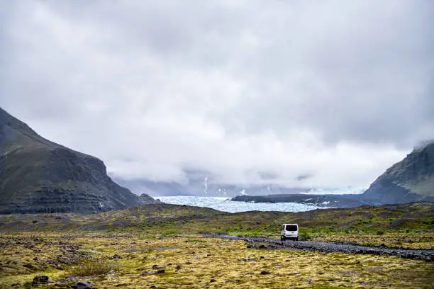 Photo of Landscape view on Skaftafell National Park, Iceland glacier tongues with tour van on gravel road and mist fog clouds in mountains