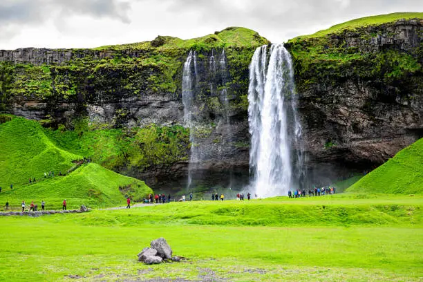 Photo of Seljalandsfoss, Iceland waterfall with white water cliff in green summer rocky landscape and people walking on trail