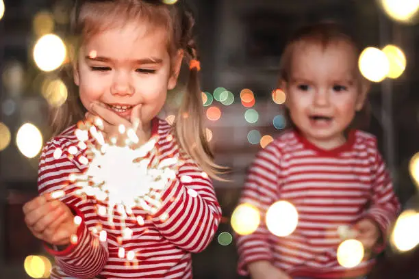 Photo of Family holidays at home. Two happy kids holding burning sparkler, indoor lifestyle