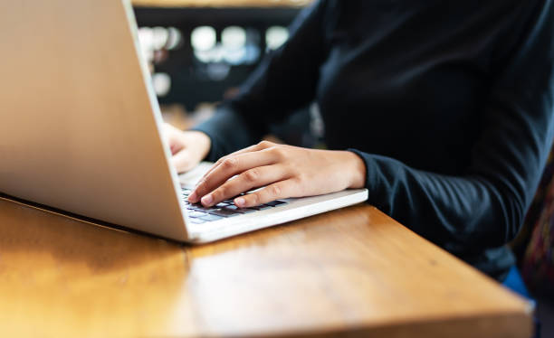 istock Asian woman using laptop at home while sitting the wooden table.hands typing on the notebook keyboard. Computer, laptop and studying remotely. 1283894379