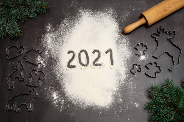 istock Numbers 2021 handwritten on flour with christmas cookie cutters, rolling pin and pine branches on dark background 1283898552