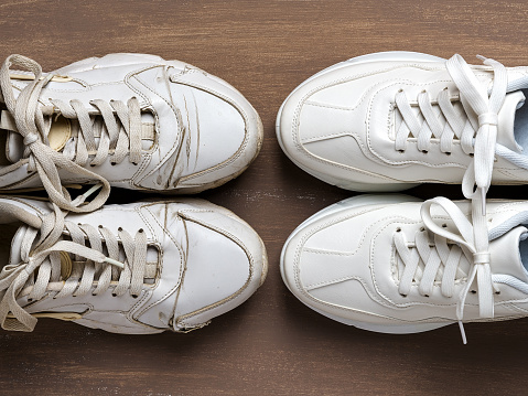 Pair of old dirty white sneakers in front of new clean one on a brown background. Past and future, old and new concepts. Comfortable shoes for active lifestyle, fitness and sports. Top view.