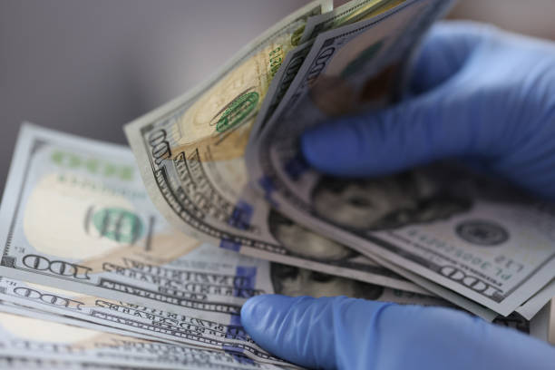 istock Hands in blue gloves hold one hundred dollar bills 1283899490