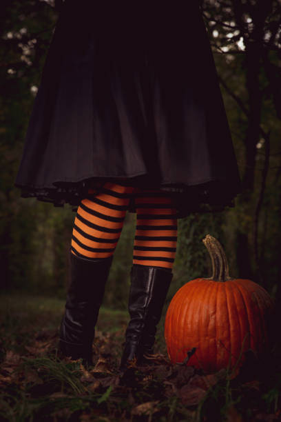 istock Witch with orange and black stockings next to a pumpkin 1283902683