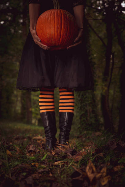 istock Witch with orange and black stockings holding a pumpkin 1283902712