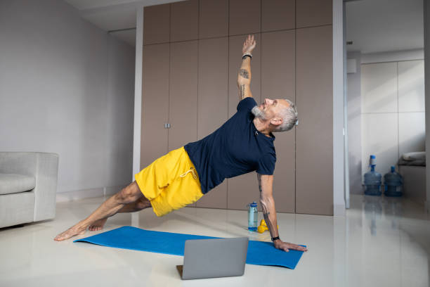 Healthy man carrying out a side plank during workout Muscular male easily holding his body above the floor while leaning on one hand and legs and lifting another arm man yoga tattoo stock pictures, royalty-free photos & images